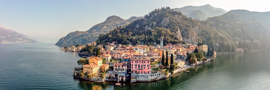 Un pueblo costero con edificios coloridos, un río y montañas al fondo.