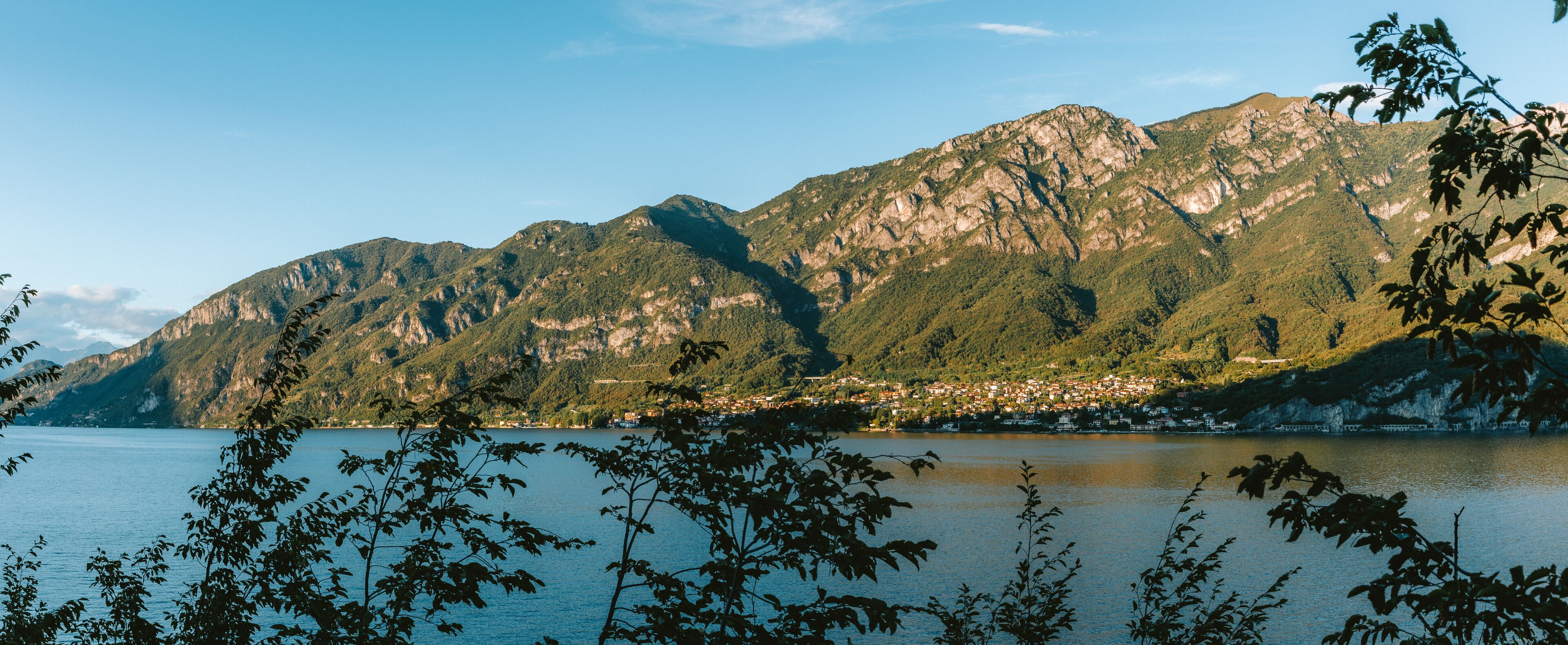 Tranquil waters reflecting the warm hues of the setting sun over a charming village on lake como, embraced by the italian alps