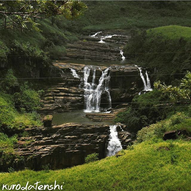 A multi-tiered waterfall cascading over rocky terrain surrounded by lush greenery.