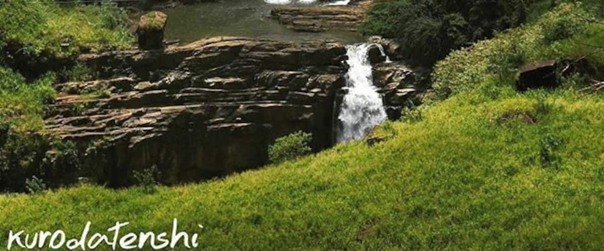 A multi-tiered waterfall cascading over rocky terrain surrounded by lush greenery.