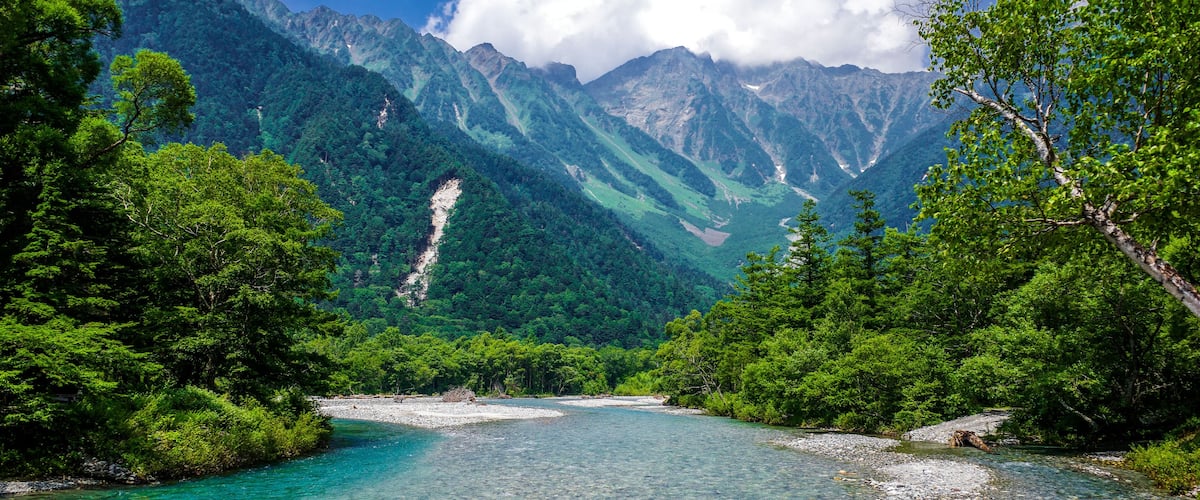 A river flowing through a mountainous landscape with dense green forests and rocky riverbanks.