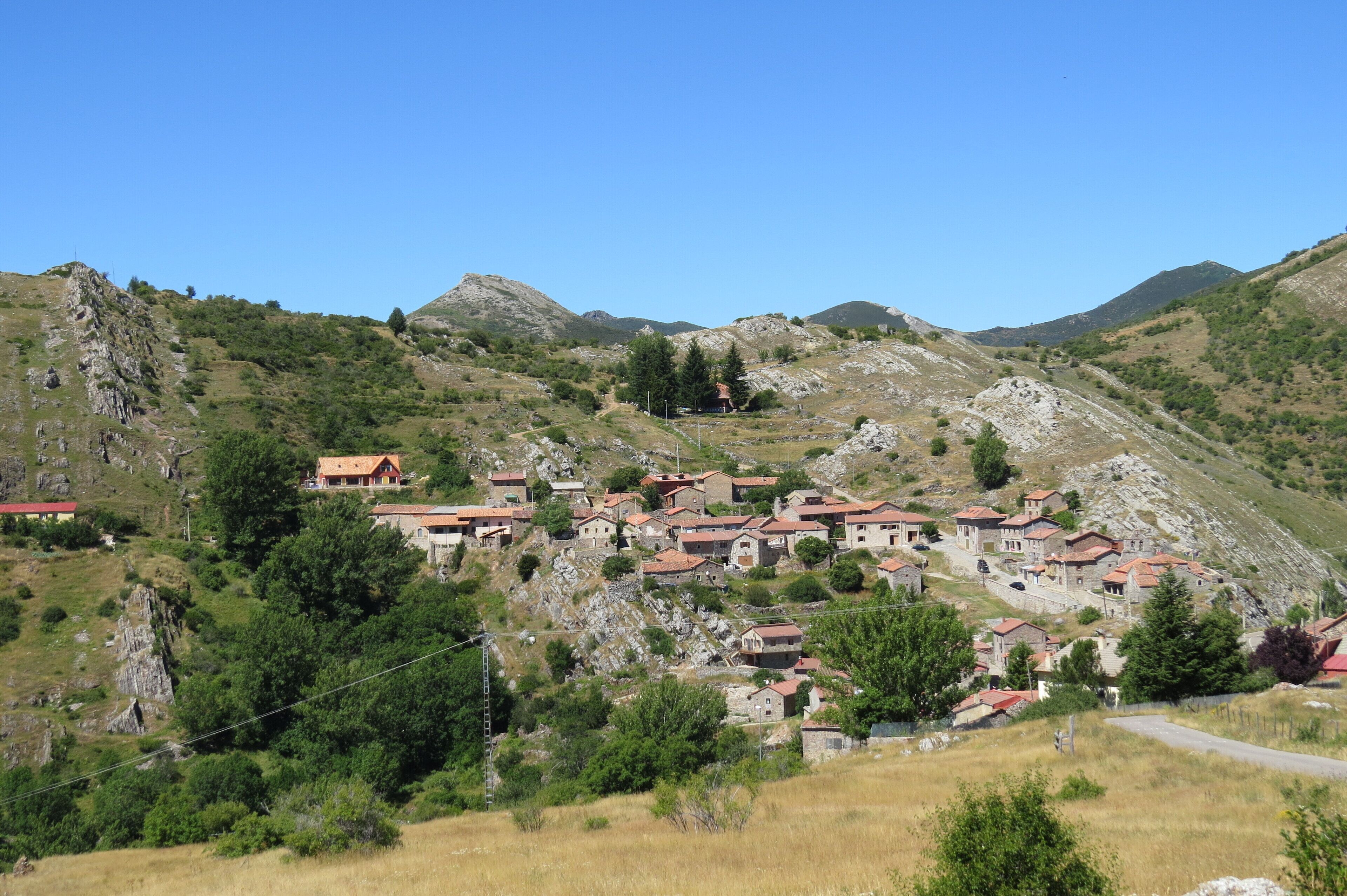 A hillside village with red-roofed houses nestled among rocky terrain and greenery.