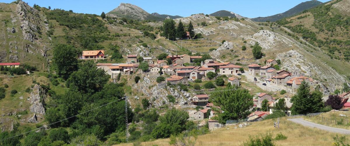 A hillside village with red-roofed houses nestled among rocky terrain and greenery.