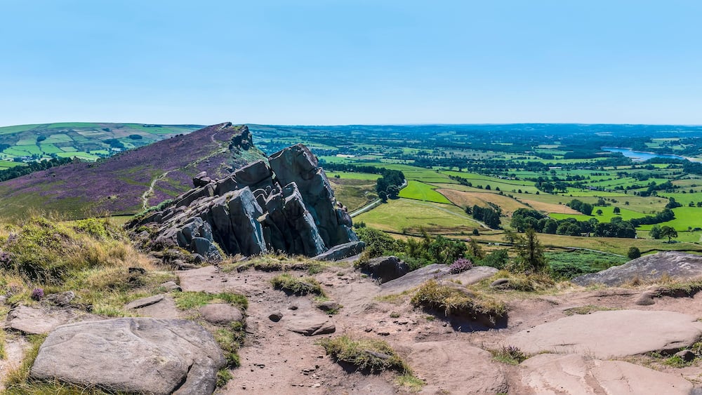 Un paysage rocheux offrant une vue sur des champs verdoyants et une rivière au loin.