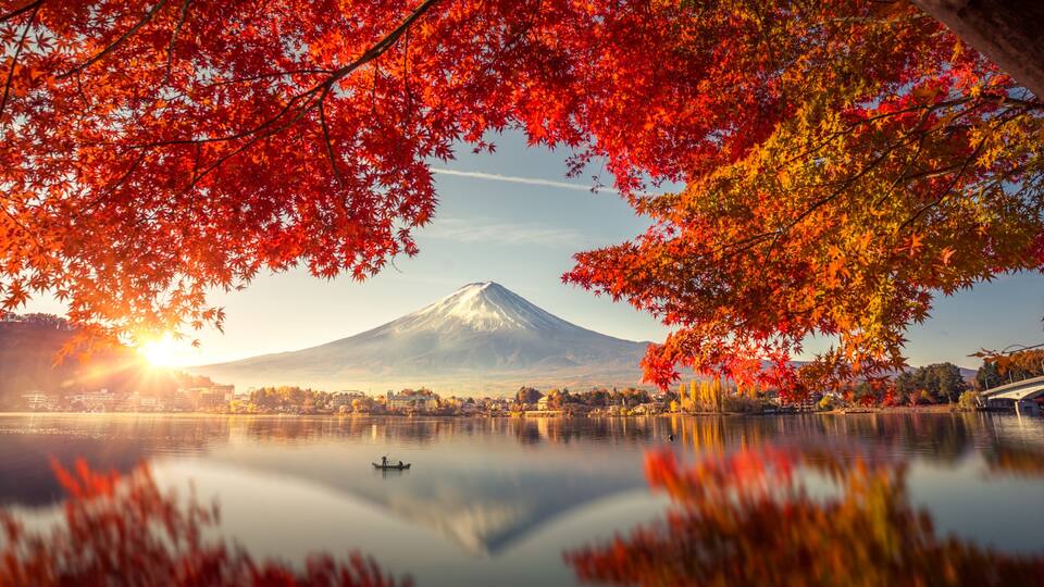 A lake with a mountain in the background, a bridge, and autumn foliage.