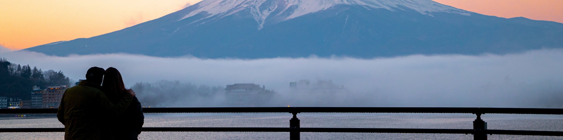 A couple overlooking a body of water with a mountain in the background.