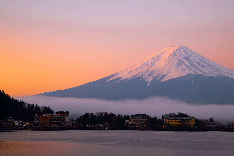 A snow-capped mountain at sunset with a town in the foreground.