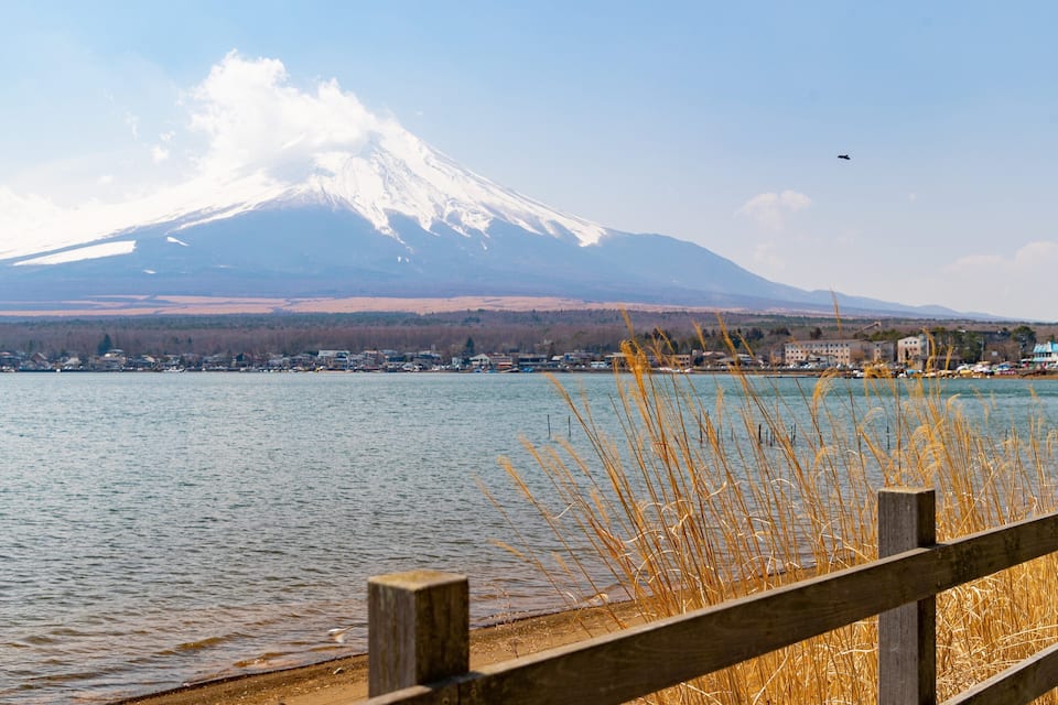 A lake with a wooden fence in the foreground, a town in the middle ground, and a snow-capped mountain in the background.