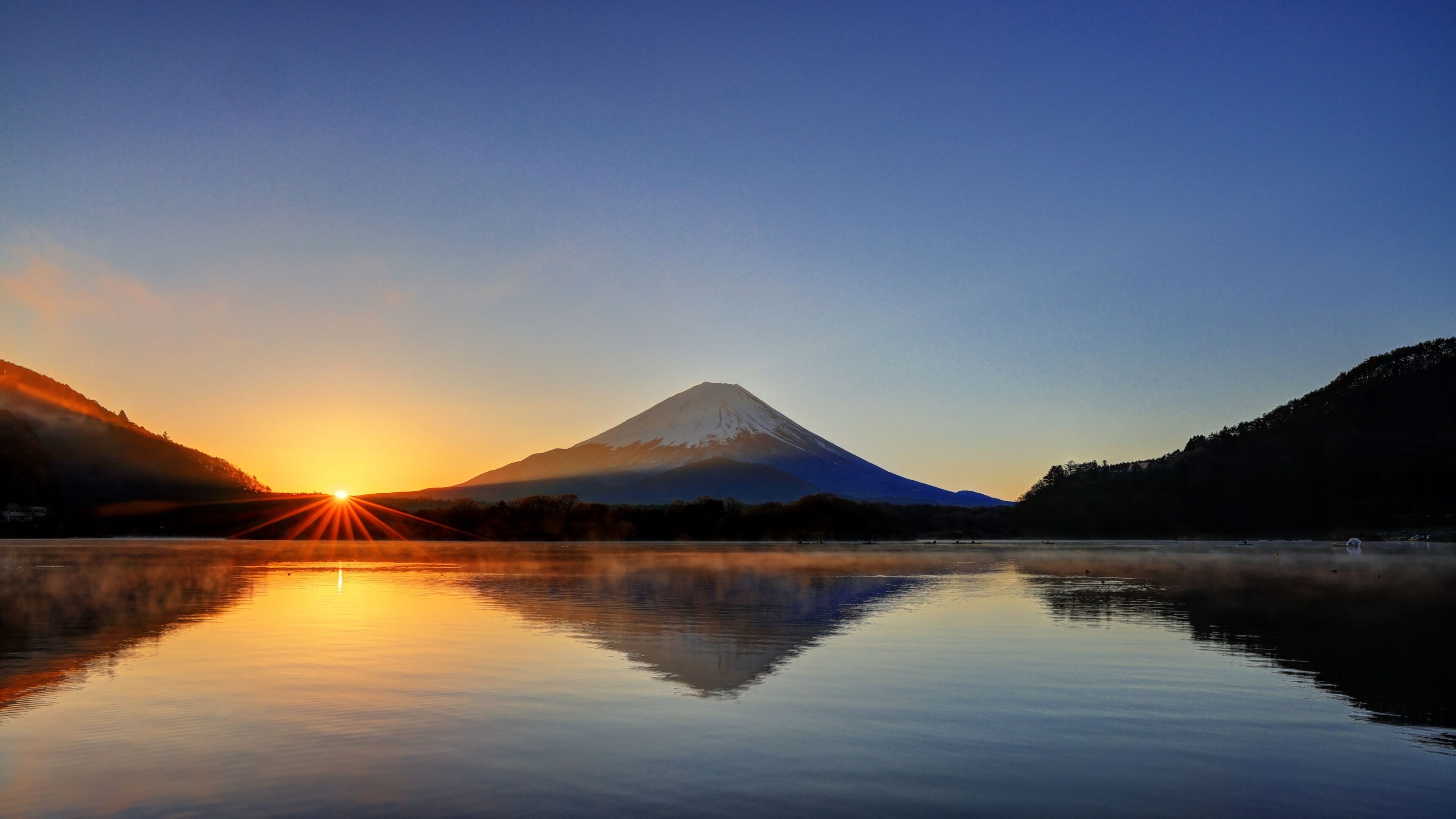 Un lac paisible, avec une montagne en arrière-plan, dont la surface reflète la lumière du soleil.