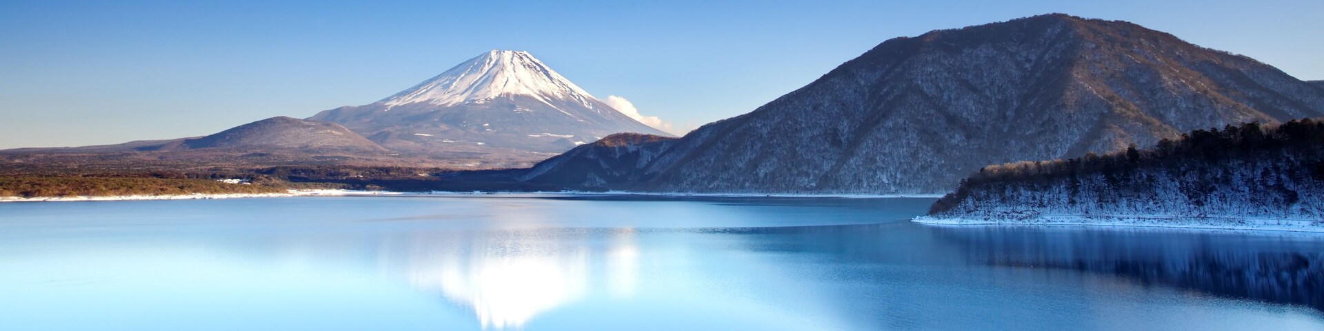 Un lago tranquilo que refleja una montaña nevada y una colina boscosa.