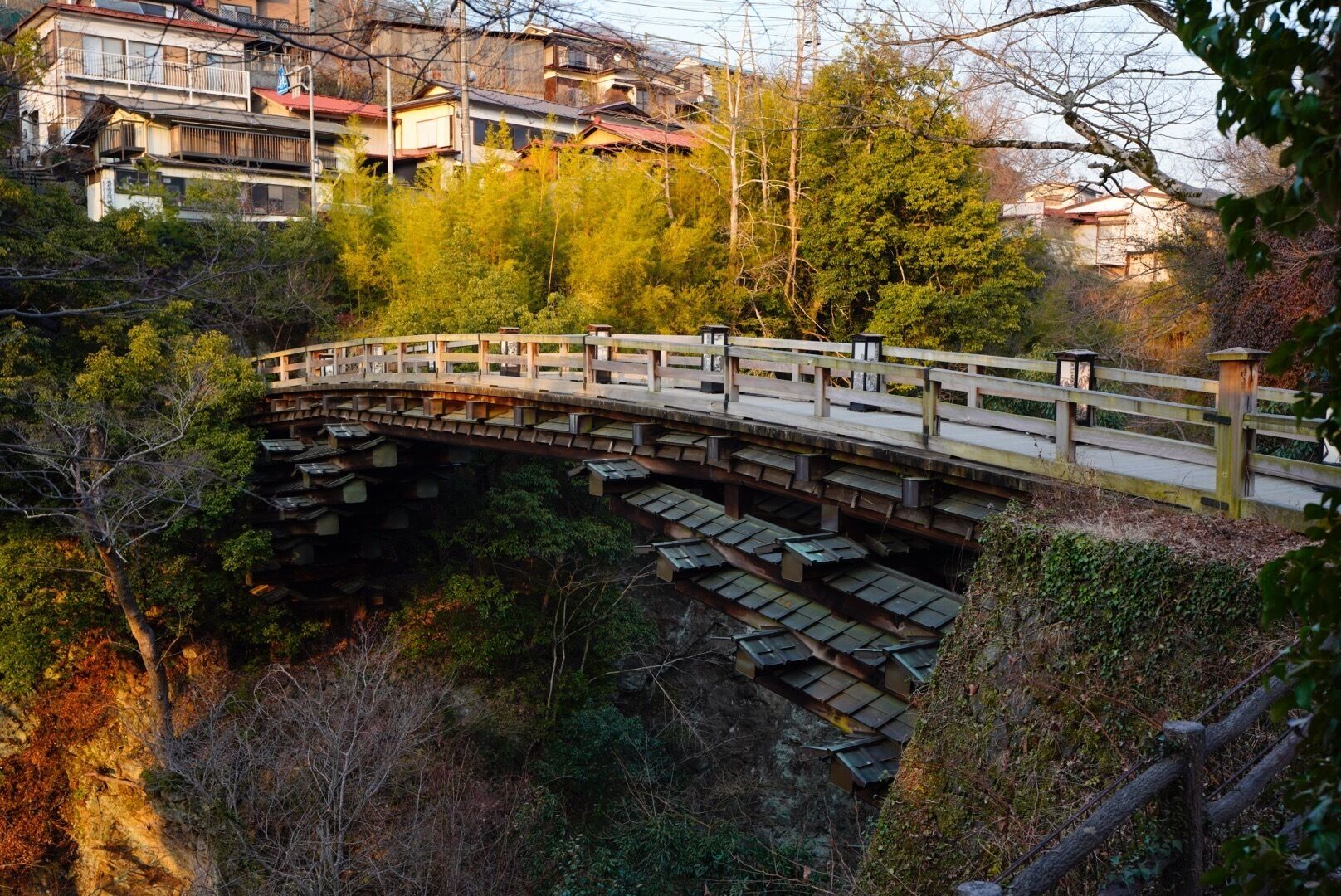 A wooden bridge over a railway track surrounded by trees and buildings.
