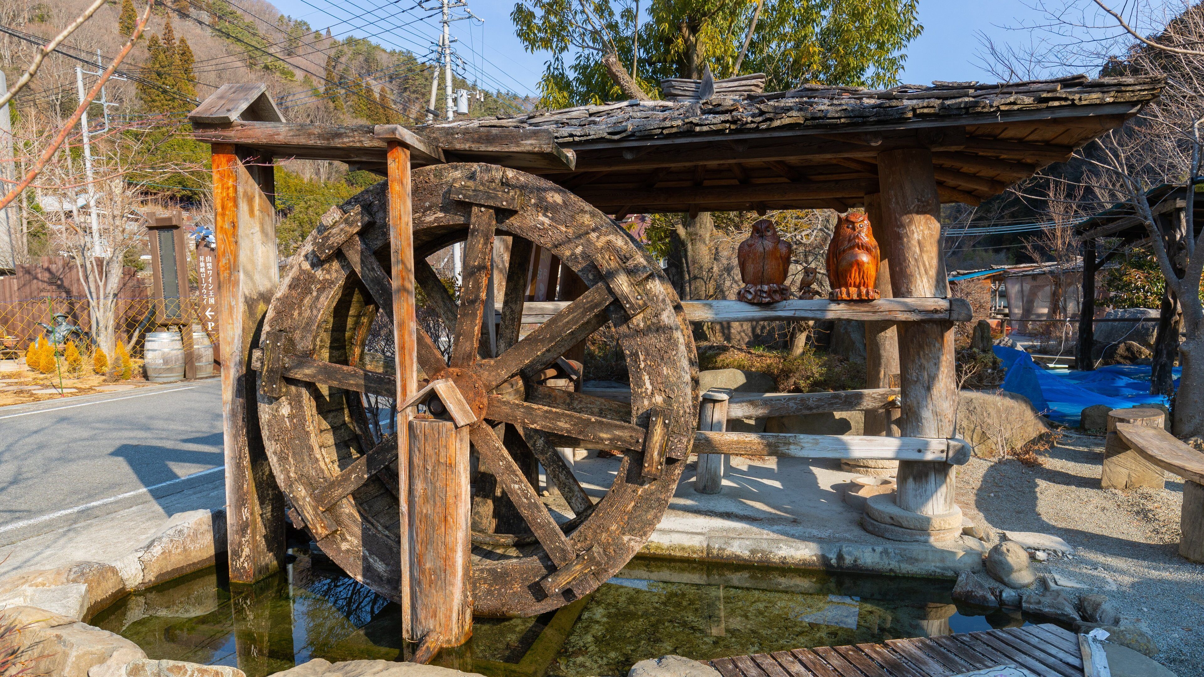 A traditional water wheel with a wooden structure and a stone basin in a rural setting.