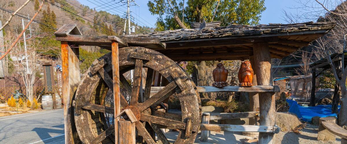A traditional water wheel with a wooden structure and a stone basin in a rural setting.