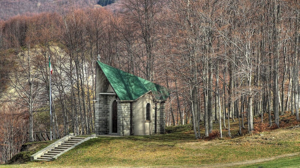 Une petite église en pierre, surmontée d’un toit vert, est entourée d’une forêt.