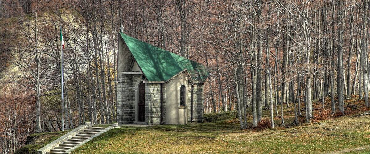 A small stone church with a green roof surrounded by a forest.