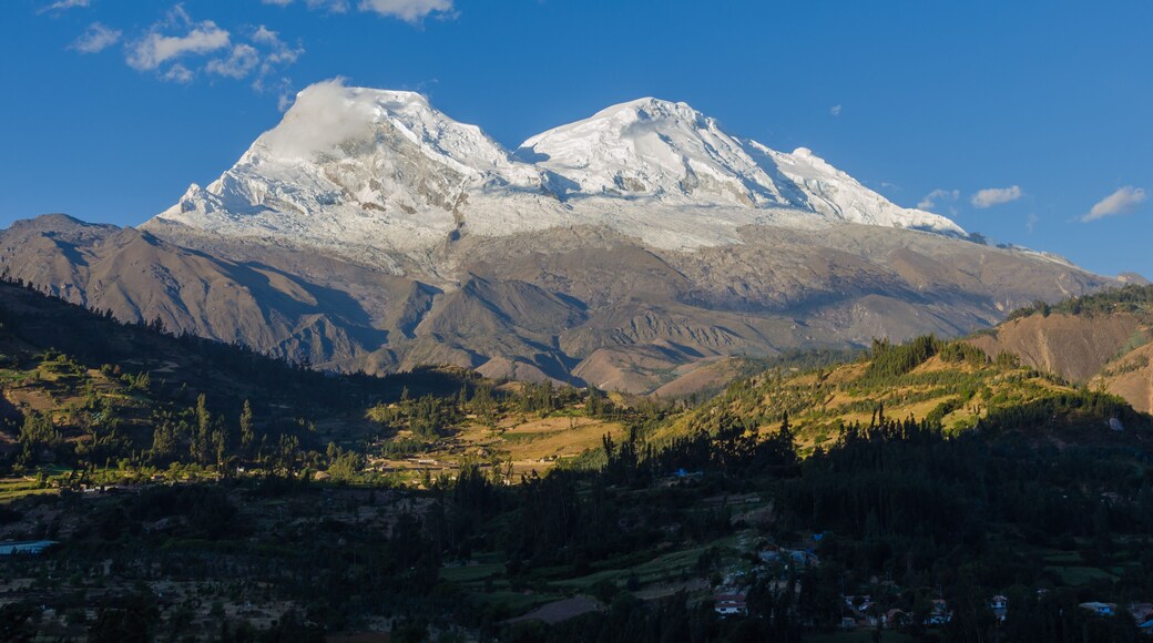 Huascaran mountain in Peru with its two snowy peaks rising over green valley where the town of Yungay sits, destroyed by a flood