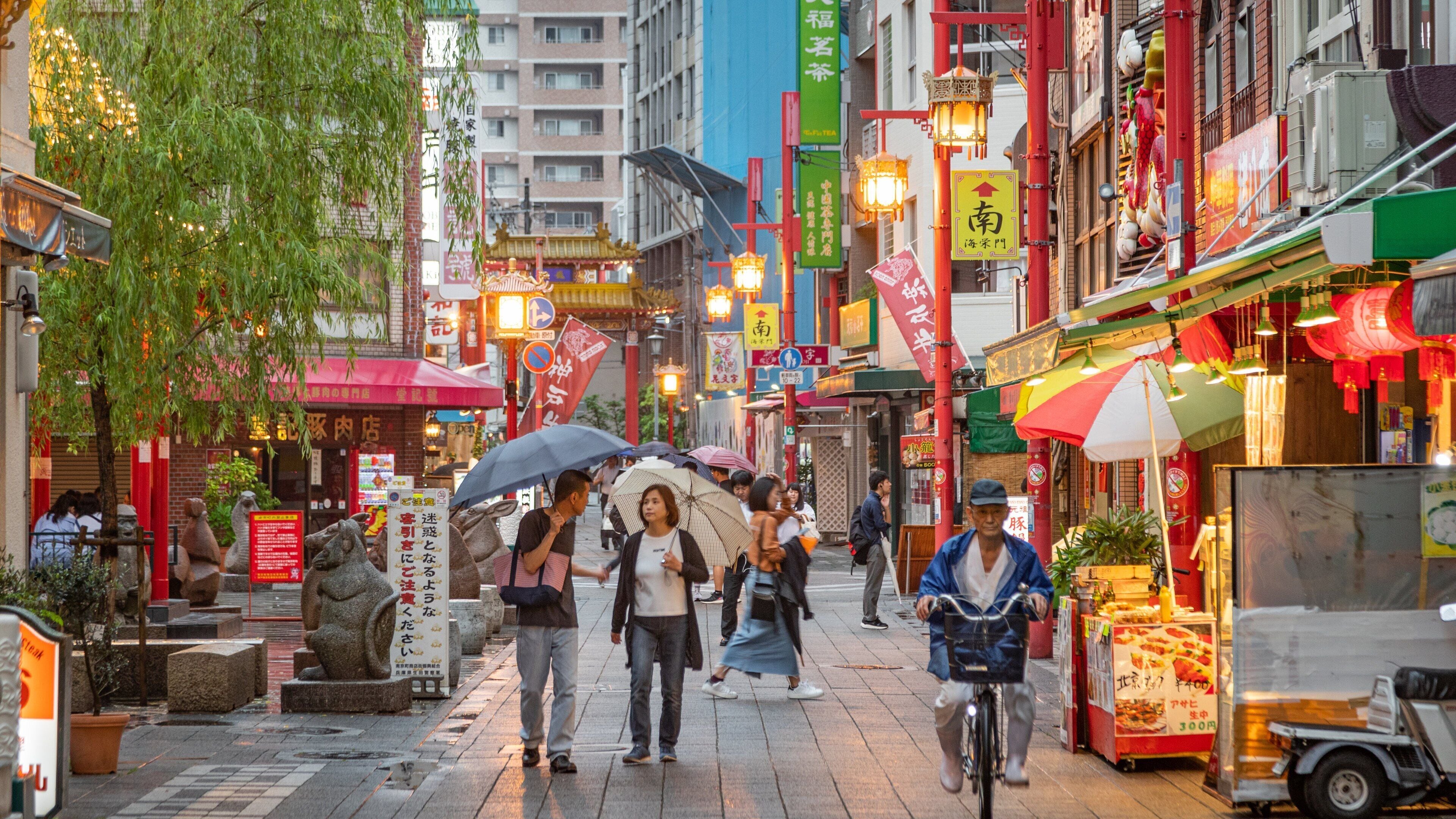A bustling street in an Asian city with traditional architecture, shops, and street vendors.