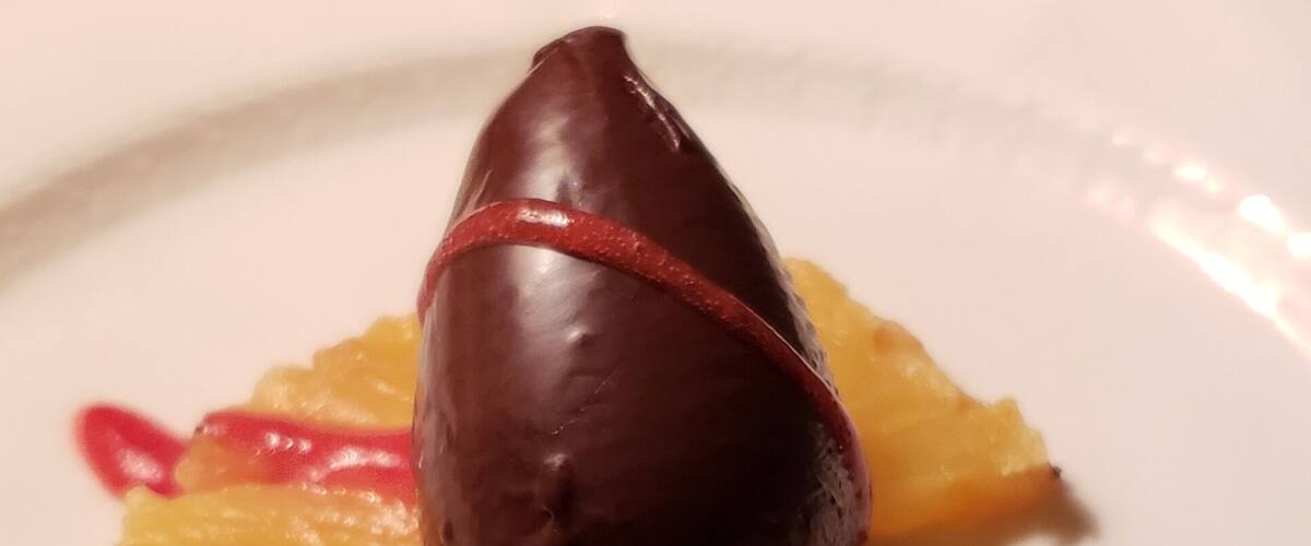 A dessert with a chocolate dome, orange slices, and a pink flower on a white plate.