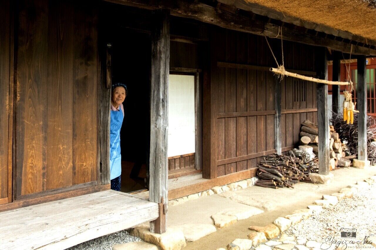 A rustic wooden house with a thatched roof, a wooden door, and a stone pathway leading to it.