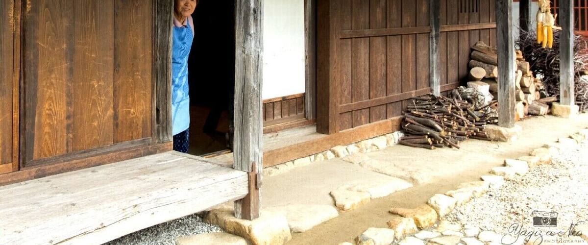 A rustic wooden house with a thatched roof, a wooden door, and a stone pathway leading to it.