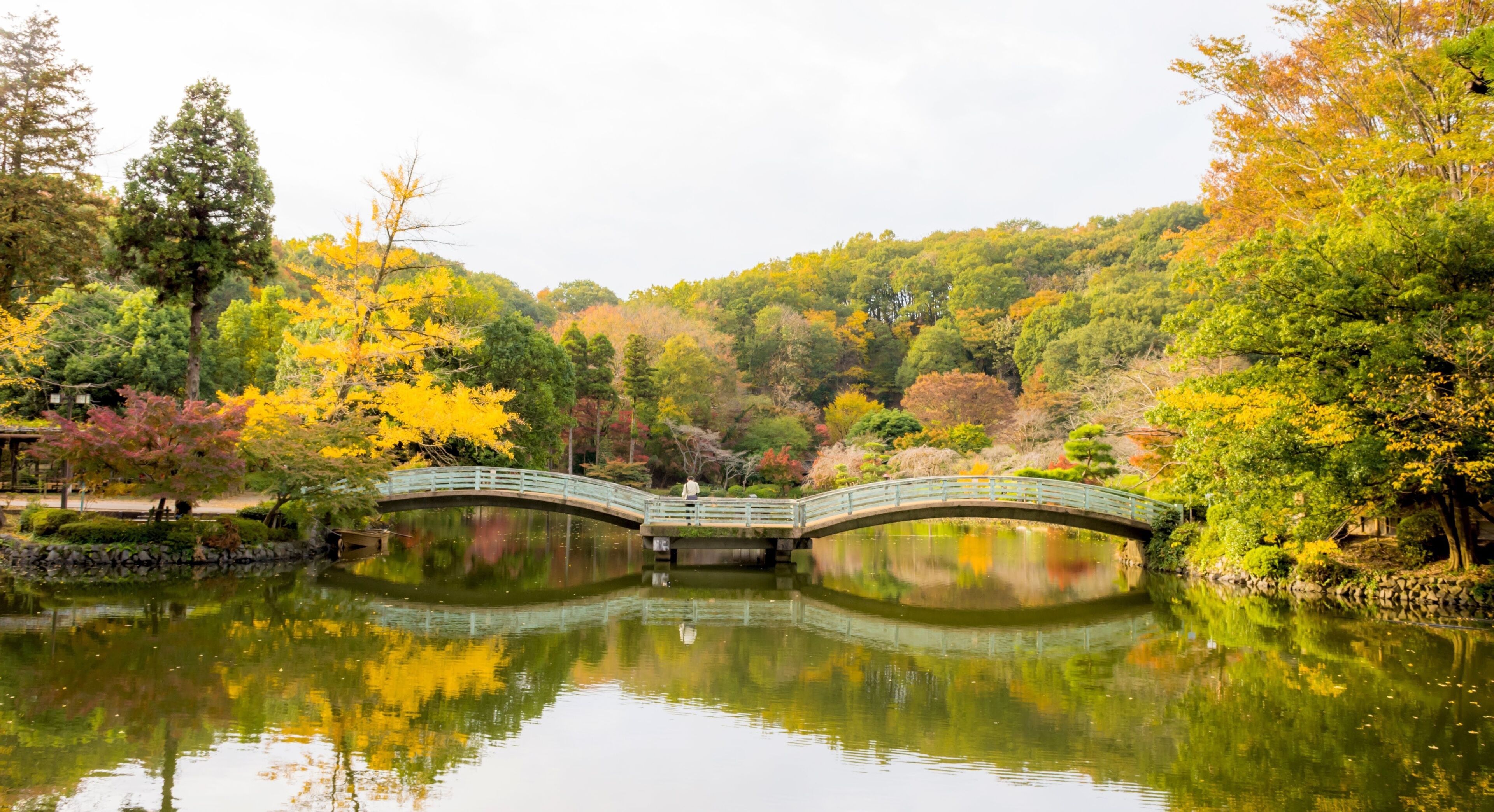 A stone bridge over a calm pond surrounded by autumn-colored trees.