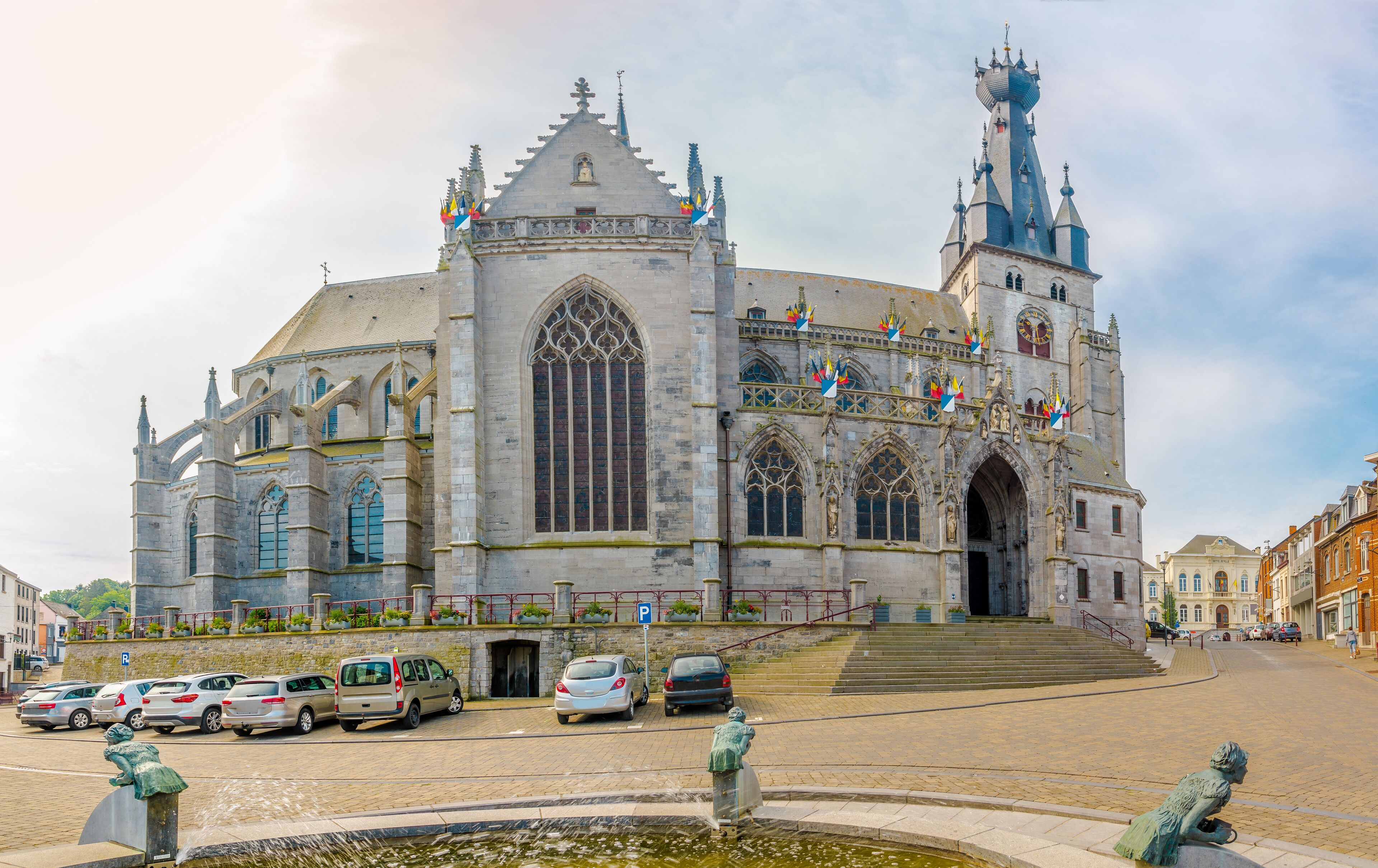A historic cathedral with Gothic architecture, a prominent clock tower, and a fountain with statues.