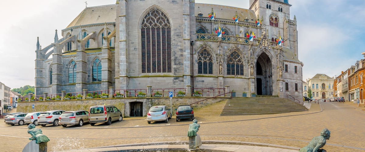 A historic cathedral with Gothic architecture, a prominent clock tower, and a fountain with statues.