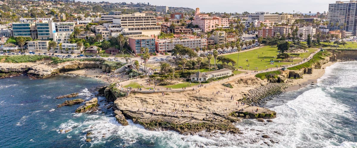 A coastal cityscape with a rocky shoreline, buildings, and a clear sky.