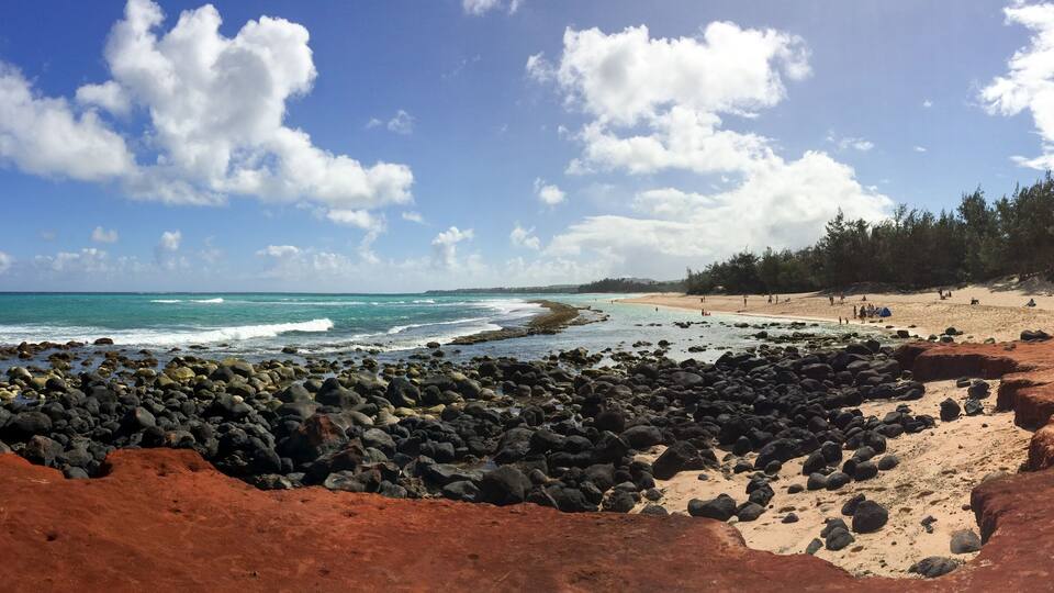 A rocky beach with waves, a clear sky, and a distant shoreline.