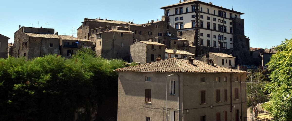 A cluster of historic buildings with terracotta roofs, surrounded by greenery.