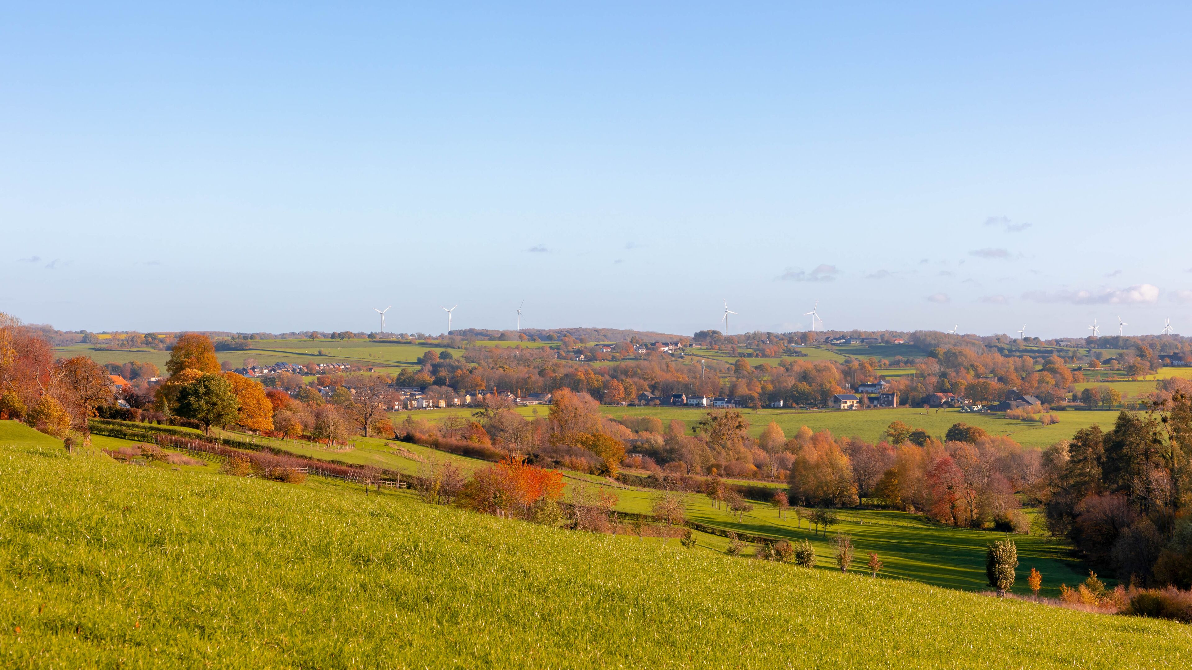 A rural landscape with rolling hills, wind turbines, and autumn-colored trees.