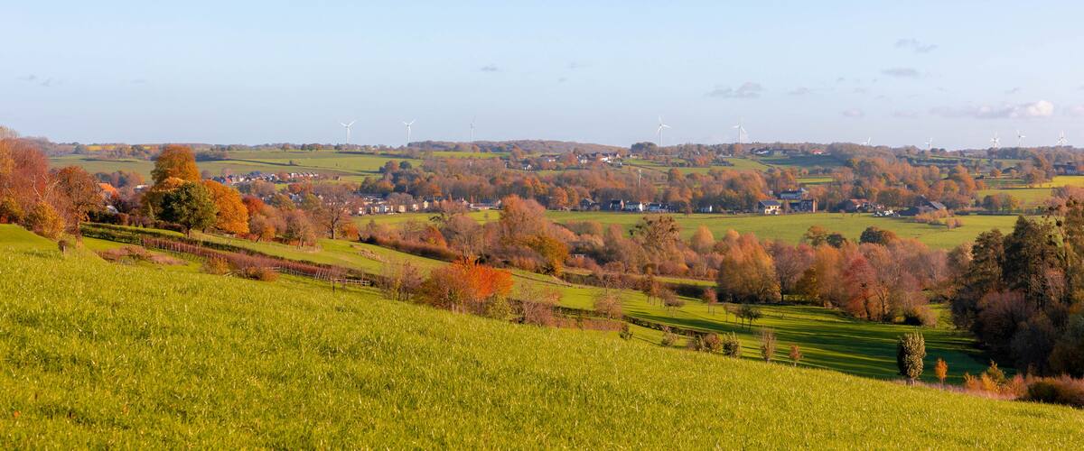 A rural landscape with rolling hills, wind turbines, and autumn-colored trees.