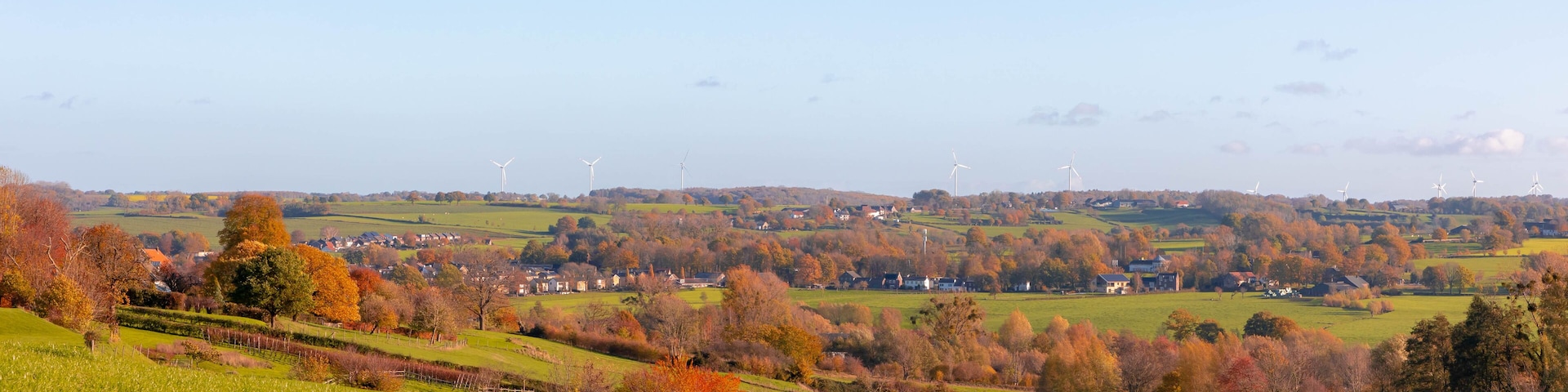 A rural landscape with rolling hills, wind turbines, and autumn-colored trees.