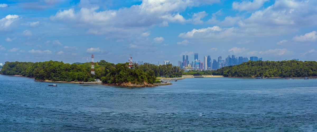 A coastal cityscape with a dense forested island and a clear blue sky.
