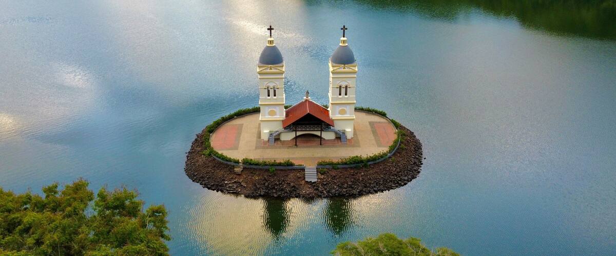 A small island with two white domed structures and a central building, surrounded by calm water and dense greenery.
