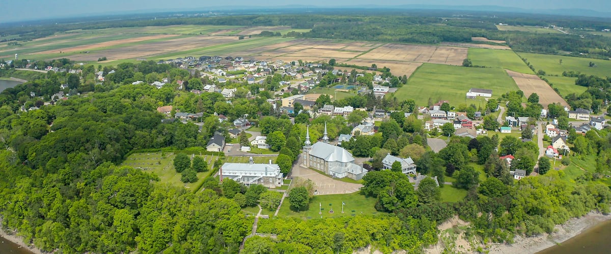 An aerial view of a riverside town with a prominent church, green fields, and a mix of residential and commercial buildings.