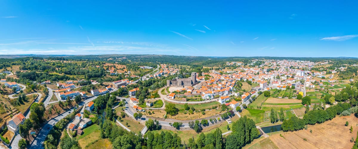 A panoramic view of a town with a prominent castle, surrounded by green fields and residential areas.