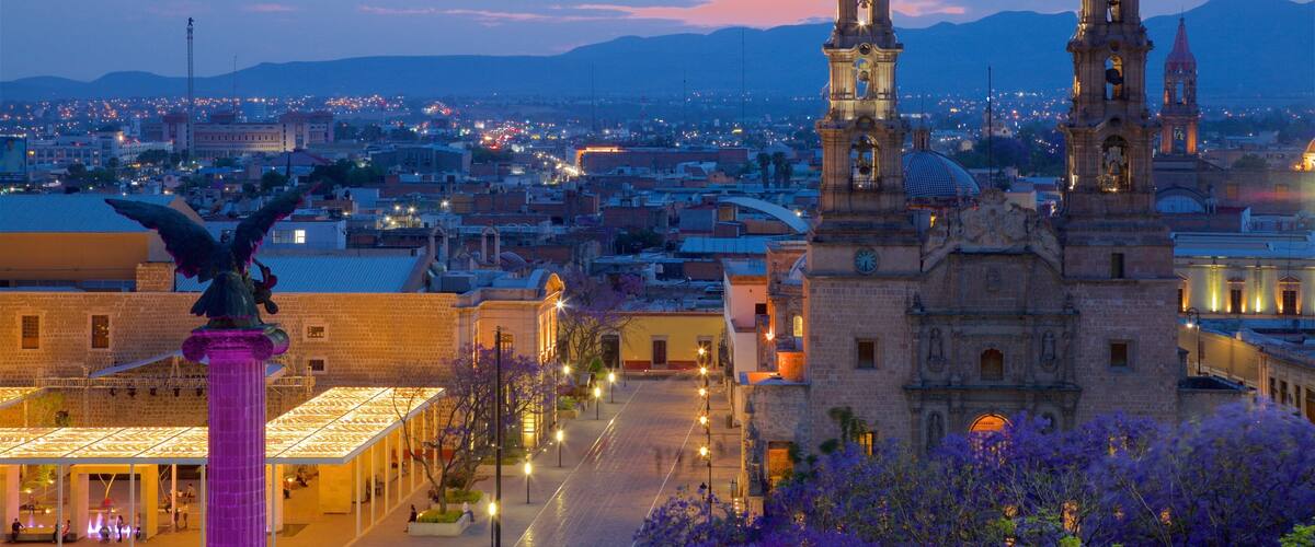 A cityscape with prominent church towers, a statue, and a well-lit plaza.
