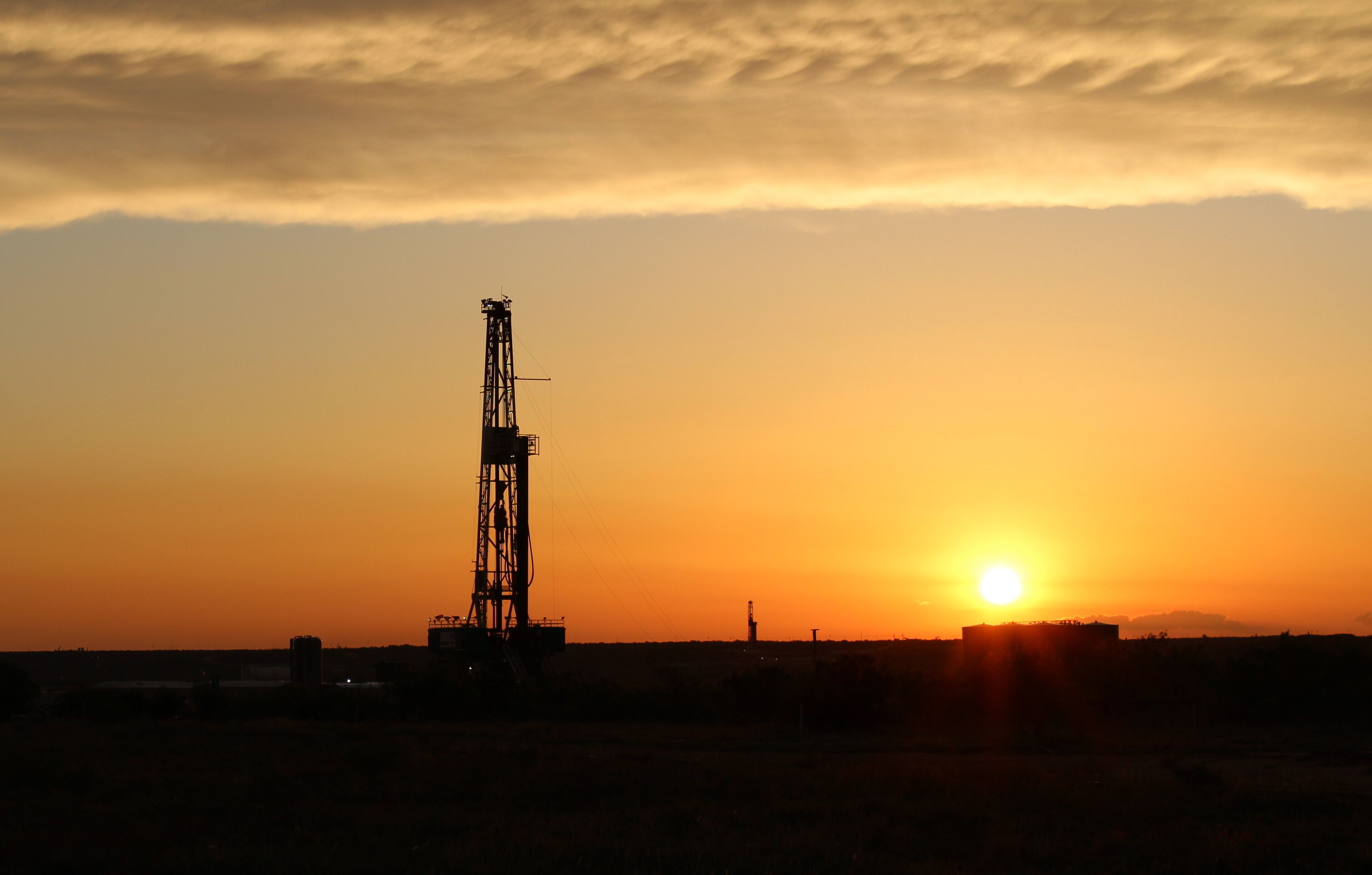 A sunset with a drilling rig silhouetted against the sky.