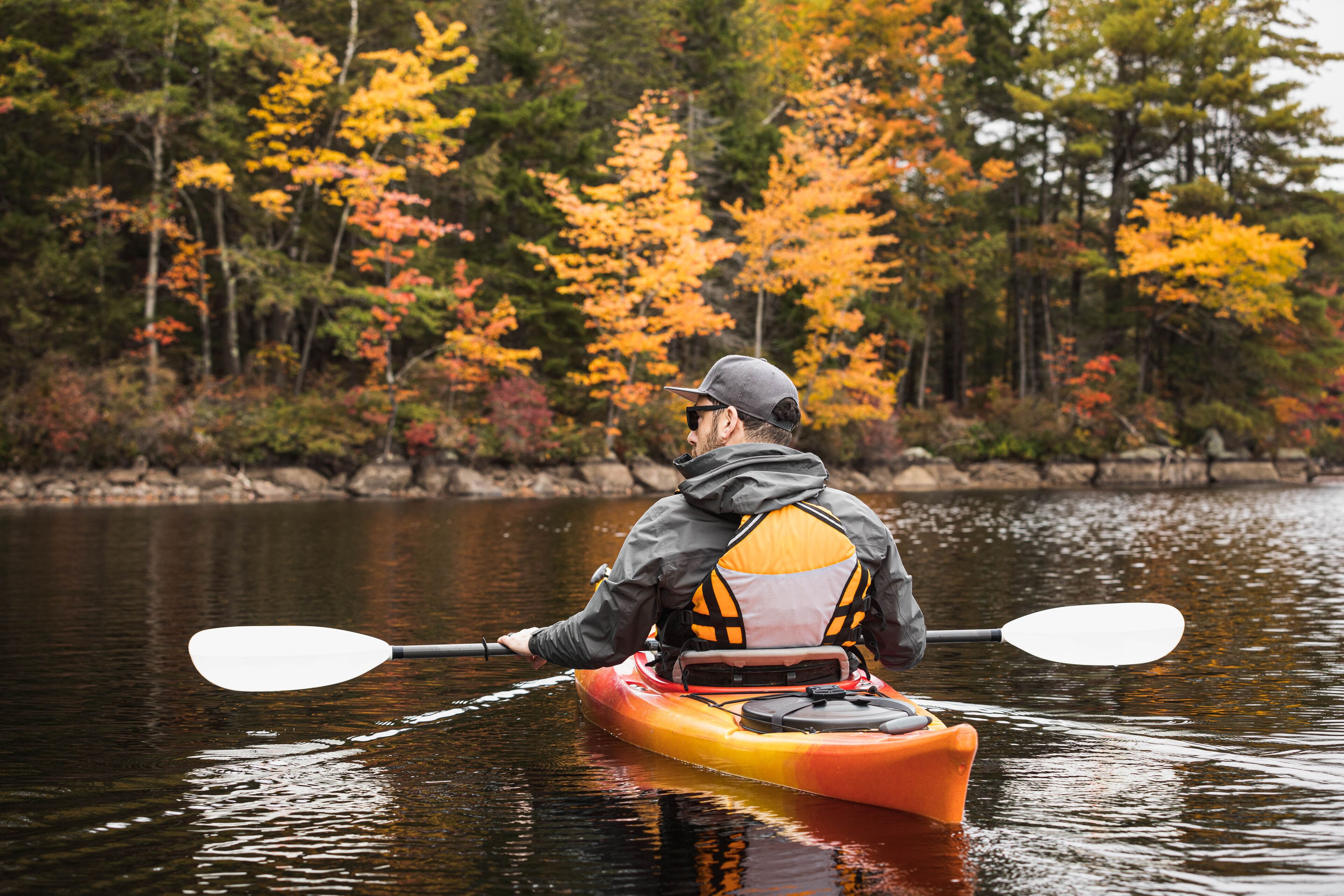 A person kayaking on a calm river surrounded by autumn-colored trees.
