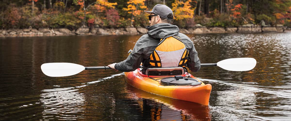 A person kayaking on a calm river surrounded by autumn-colored trees.