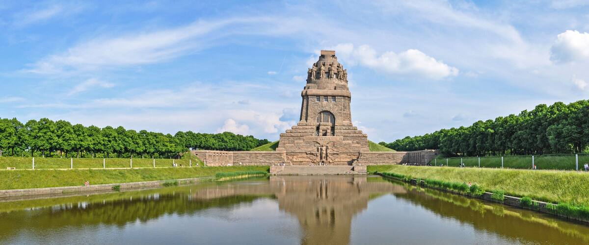 A large stone monument with a central tower, surrounded by a calm water body and lush greenery.
