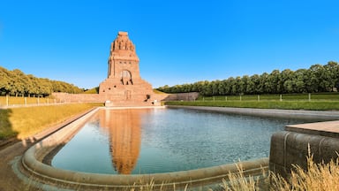 A large, ancient stone structure with a central tower, surrounded by a calm water body and a grassy area with trees.