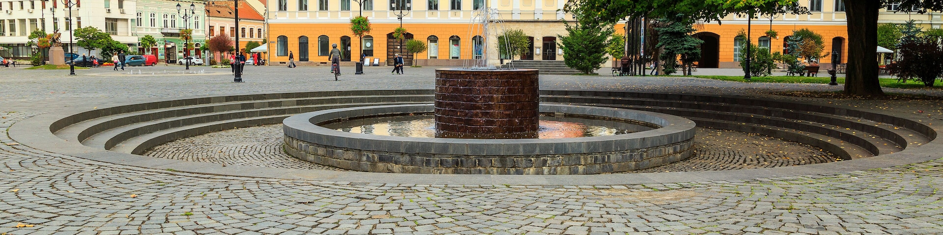 A cobblestone square with a central fountain, surrounded by historic buildings with red roofs.