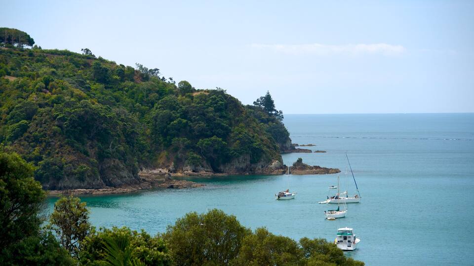 A coastal landscape with a rocky cliff, clear turquoise waters, and several sailboats anchored near the shore.