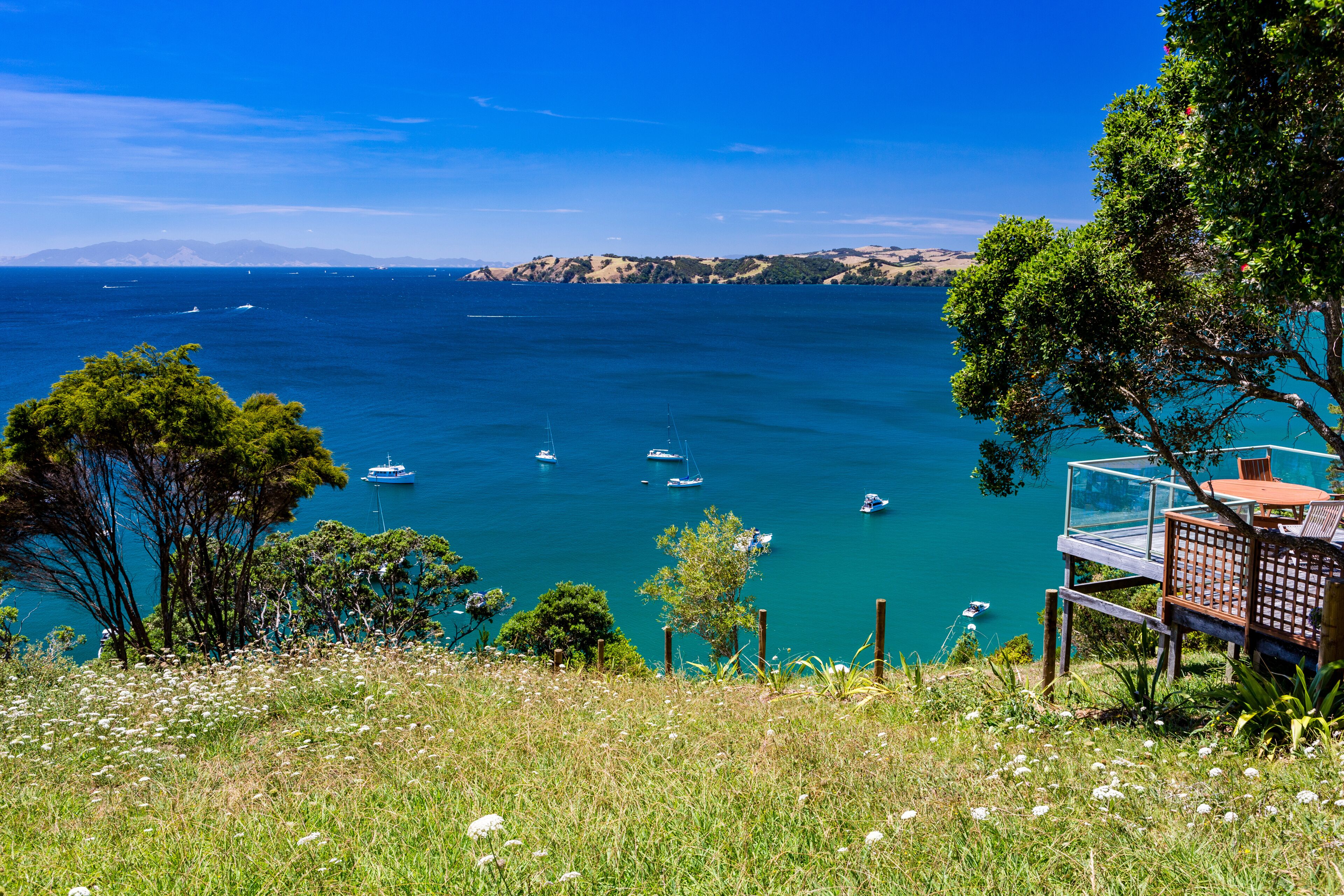 A coastal landscape with a clear blue sea, boats, and a wooden deck overlooking the water.