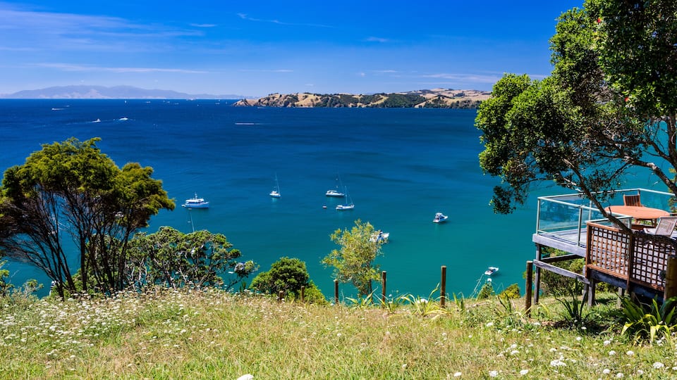 A coastal landscape with a clear blue sea, boats, and a wooden deck overlooking the water.