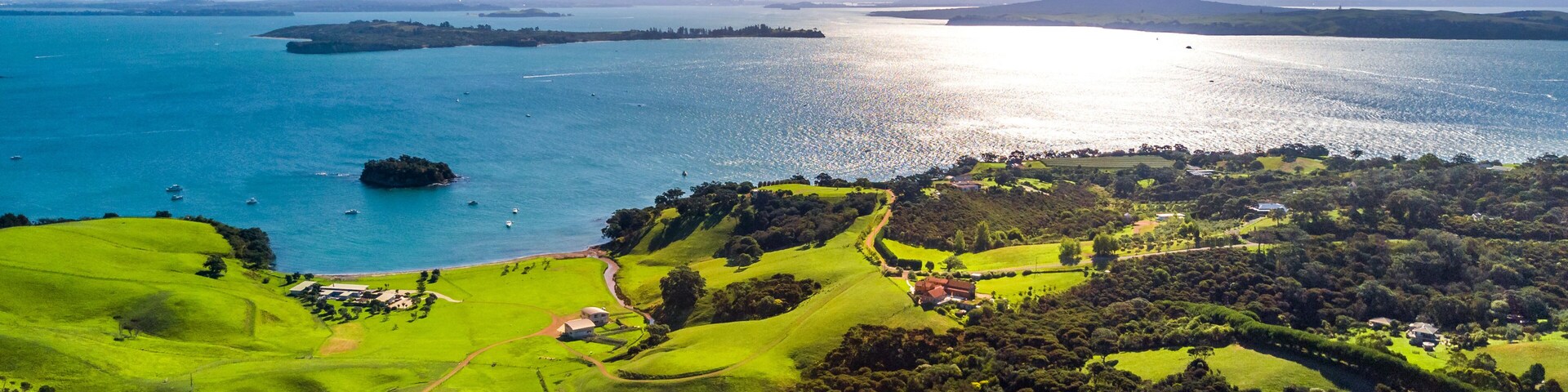 Un paisaje costero con campos verdes, una masa de agua y montañas a lo lejos.