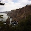A coastal landscape with rugged cliffs, dense greenery, and a calm sea.