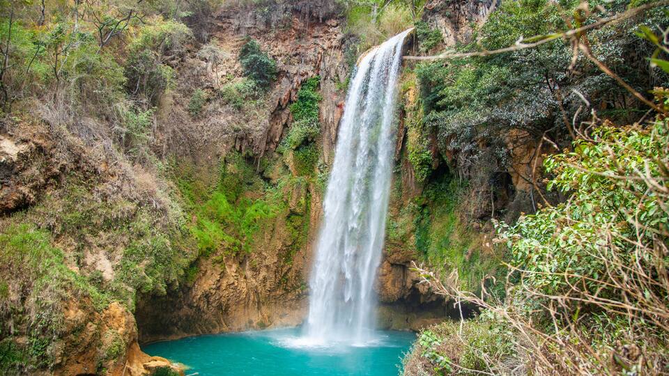 A waterfall cascading into a turquoise pool surrounded by rocky cliffs and greenery.
